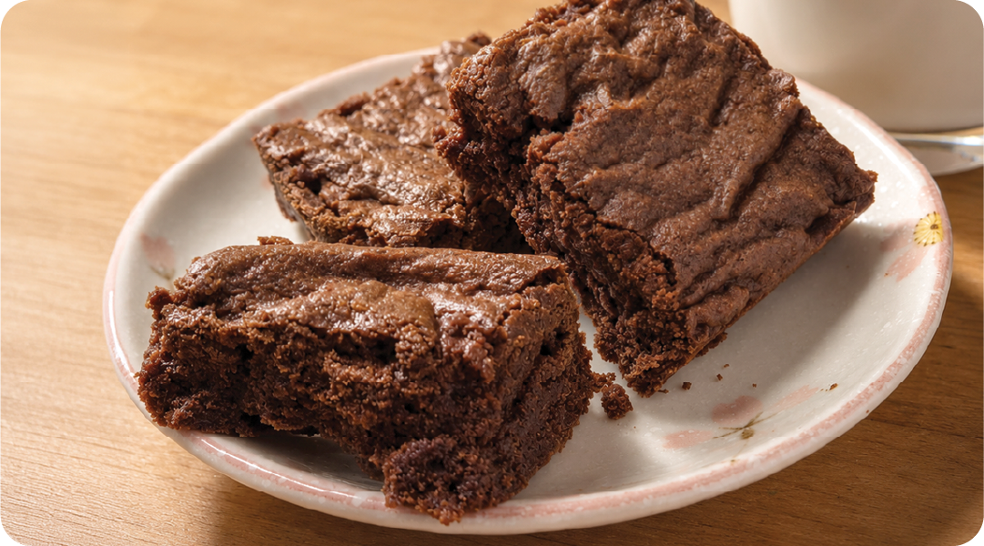 Homemade chocolate brownies stacked on a plate, showing their rich, fudgy centers and crackled tops next to a glass of milk.