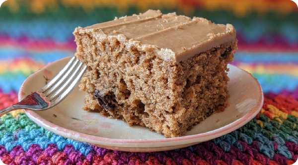 Slice of applesauce raisin cake topped with caramel frosting and served on a plate on a colorful background.